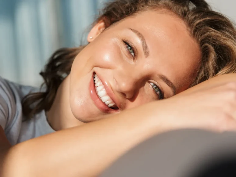 A relaxed woman smiling warmly while resting her head on her arm